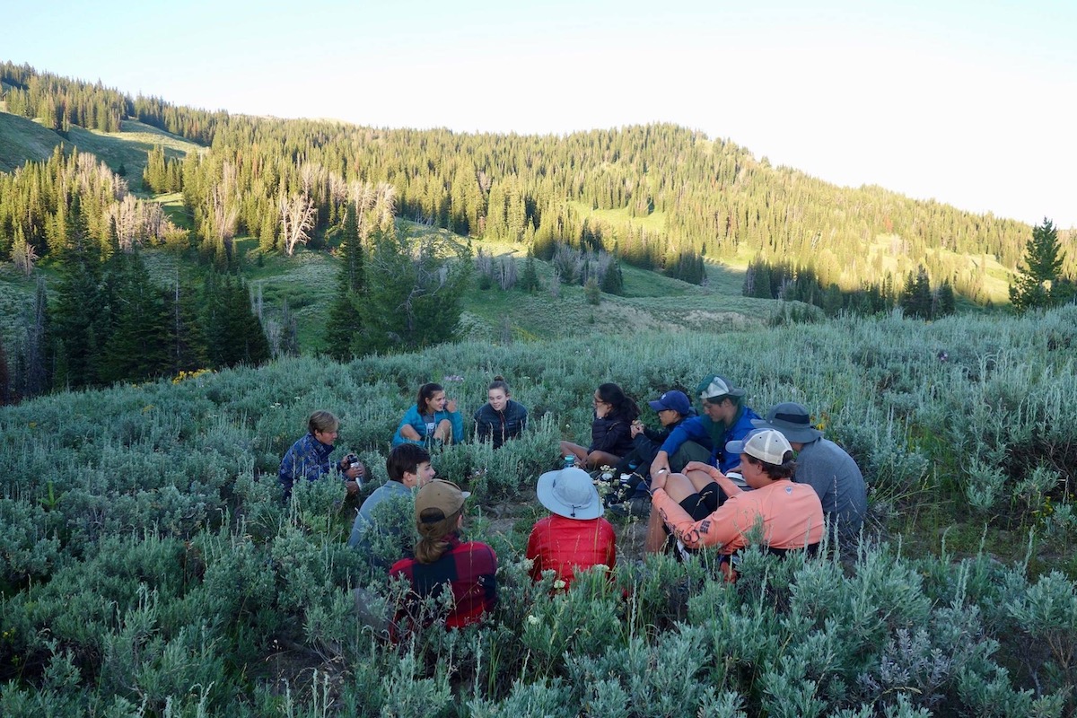 Group of NOLS students sits in a circle in sagebrush