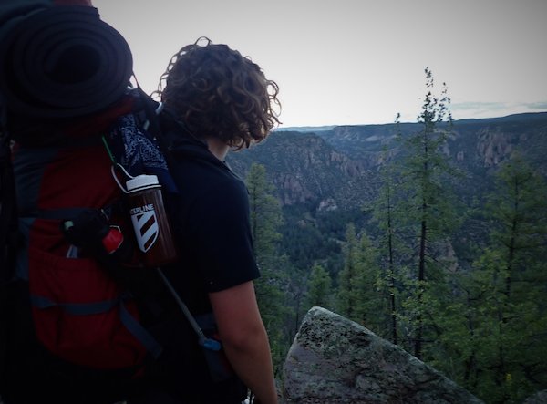NOLS backpacking student pauses to enjoy a view of trees and mountains
