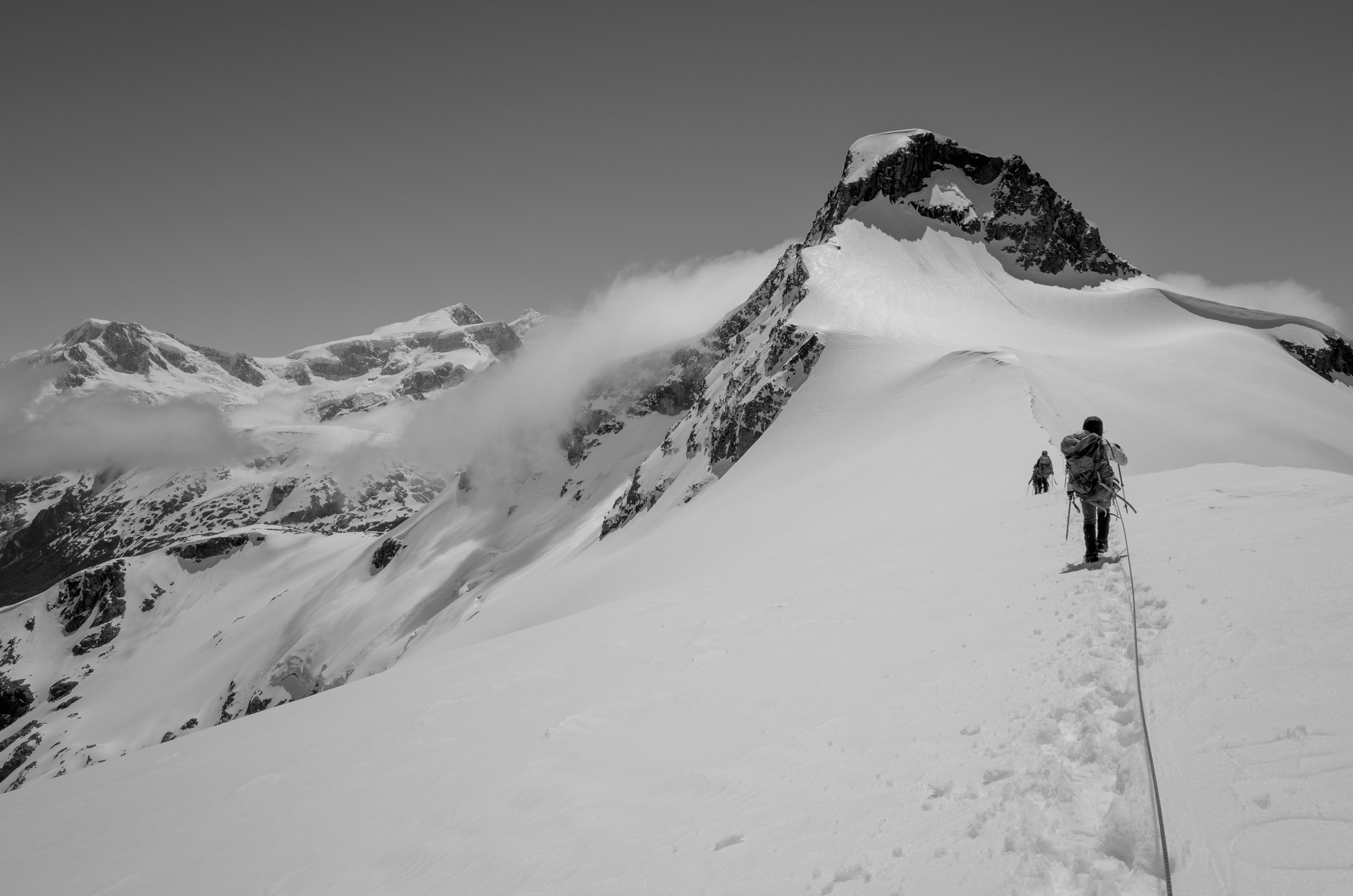 People hiking to the top of a mountain on a snow field
