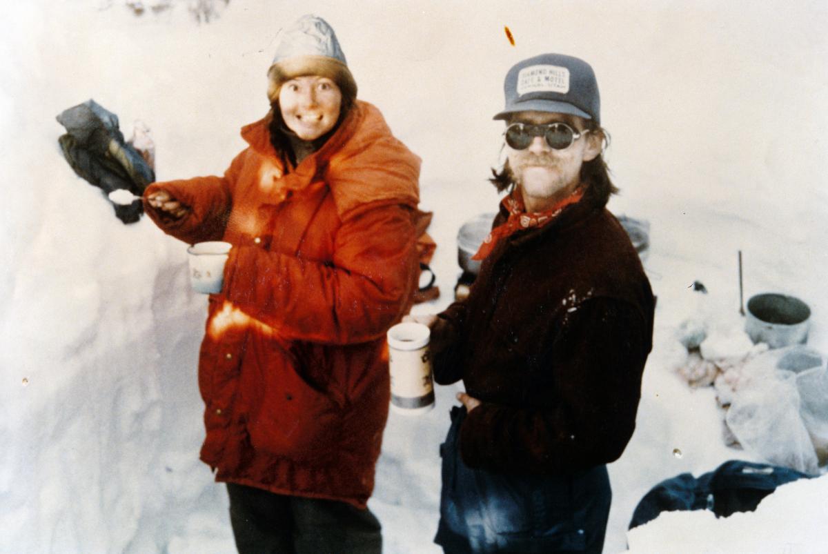 two NOLS participants on a winter course in the 1970s smile at the camera in a snow kitchene 