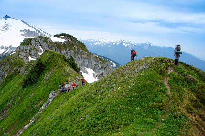 Students backpacking on scenic green hills amidst the snowy peaks of the North Cascades.