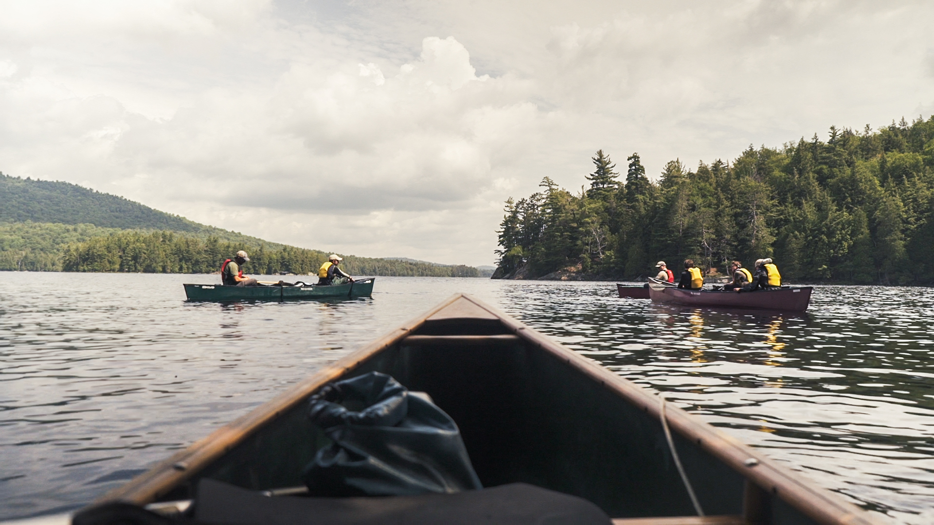 Three canoes on a lake with green islands on the left and right.