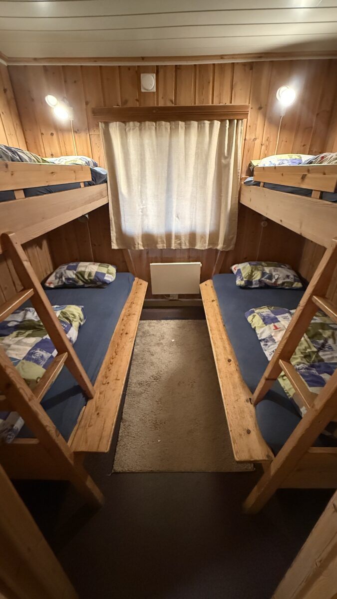Two sets of bunk beds in a cabin with blue blankets and multicolored pillows.