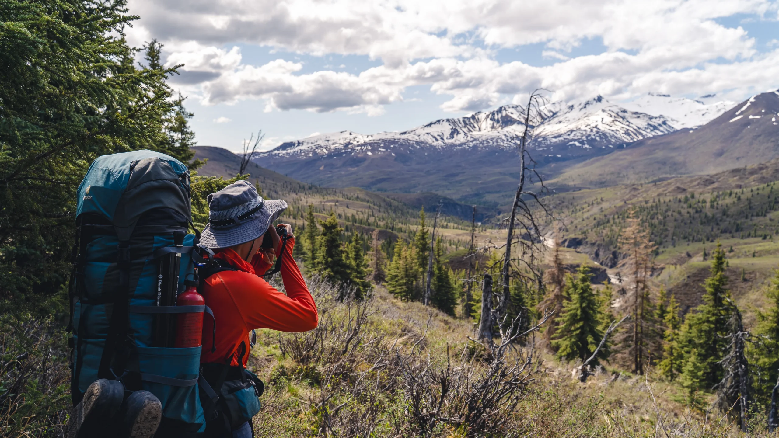 A backpacker uses binoculars to look at mountains in the distance