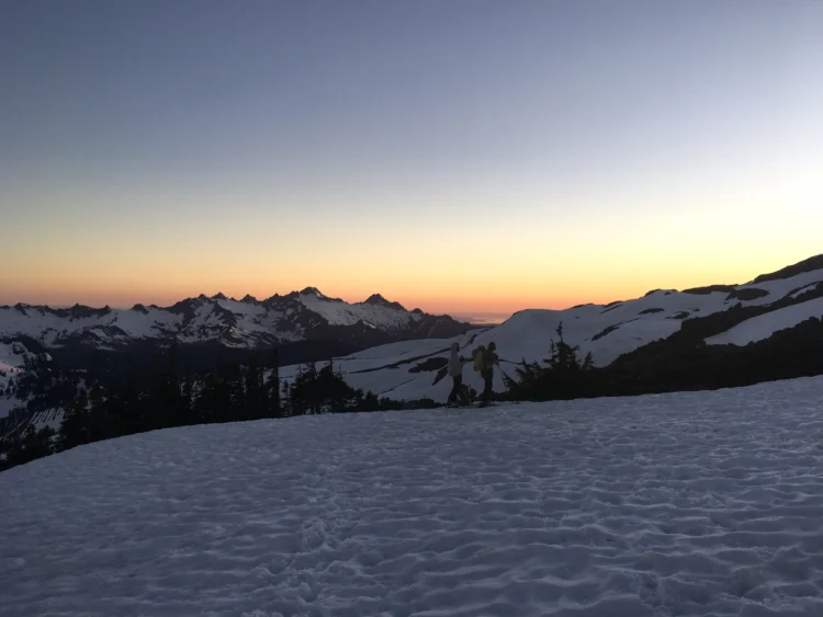 sunrise partway up a mountain. there are other mountains in the background and snow in the foreground.