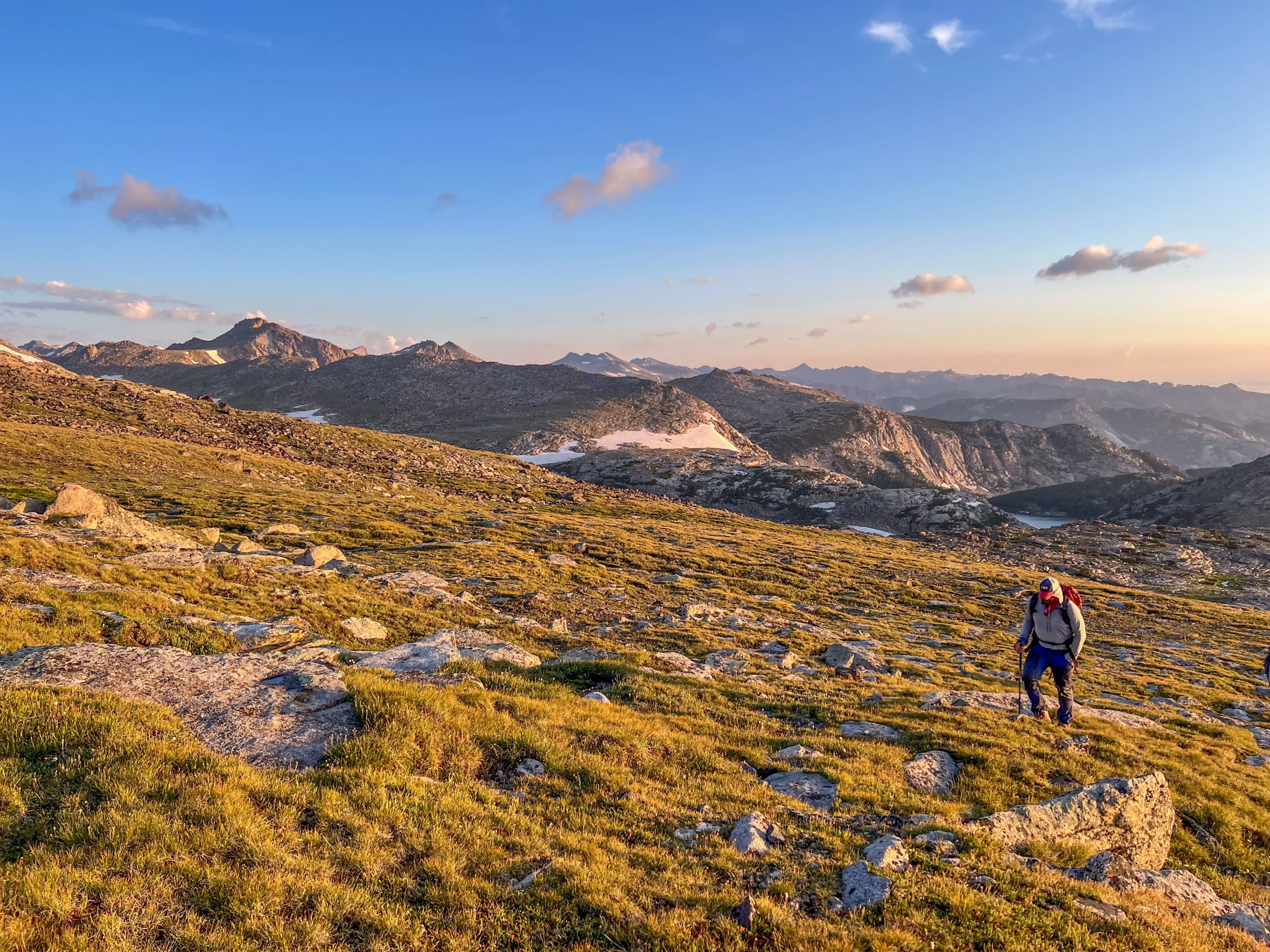 a person hikes up a gentle mountain slope at sunset. there are granite peaks and ponds in the background.