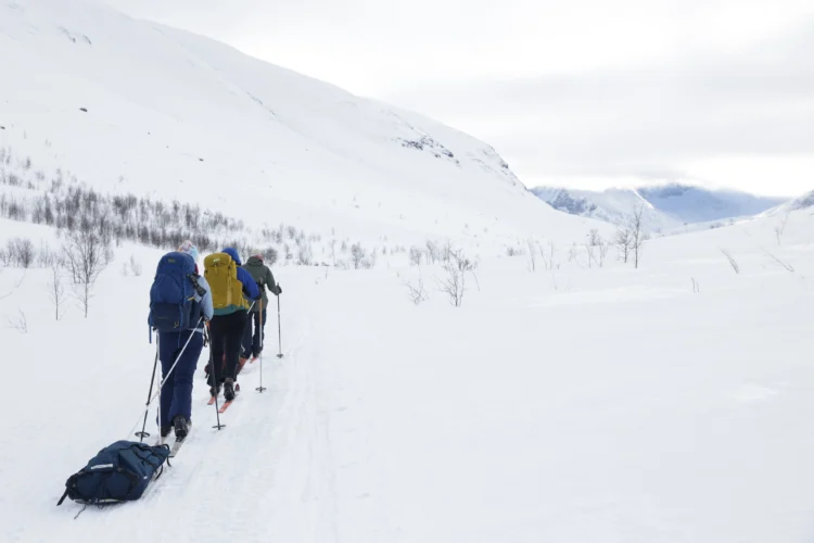 Skiers slide along the tundra carrying a sled of gear.