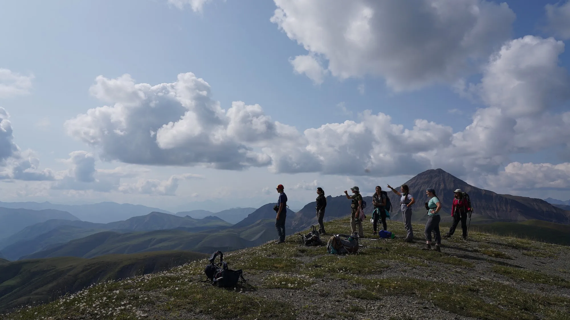 a group of people stand on a grassy hill looking out over a valley.