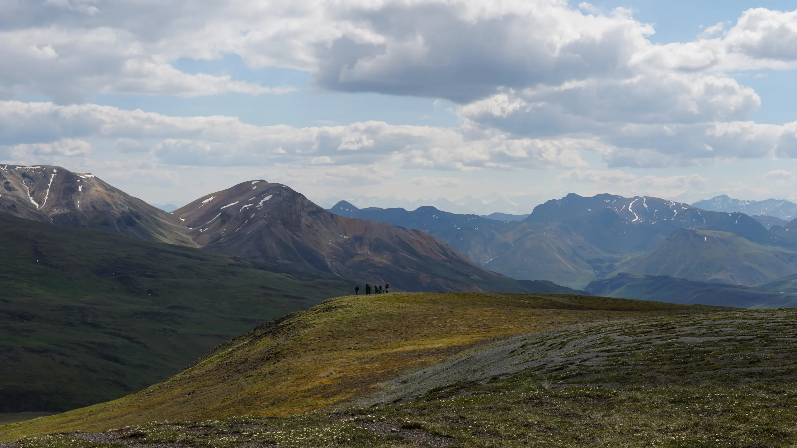 grassy mountain tops with jagged peaks and cloudy sky in the background.