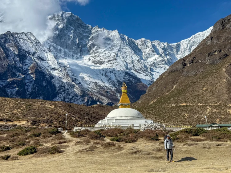 A temple stands at the base of the mountains with a hiker looking on