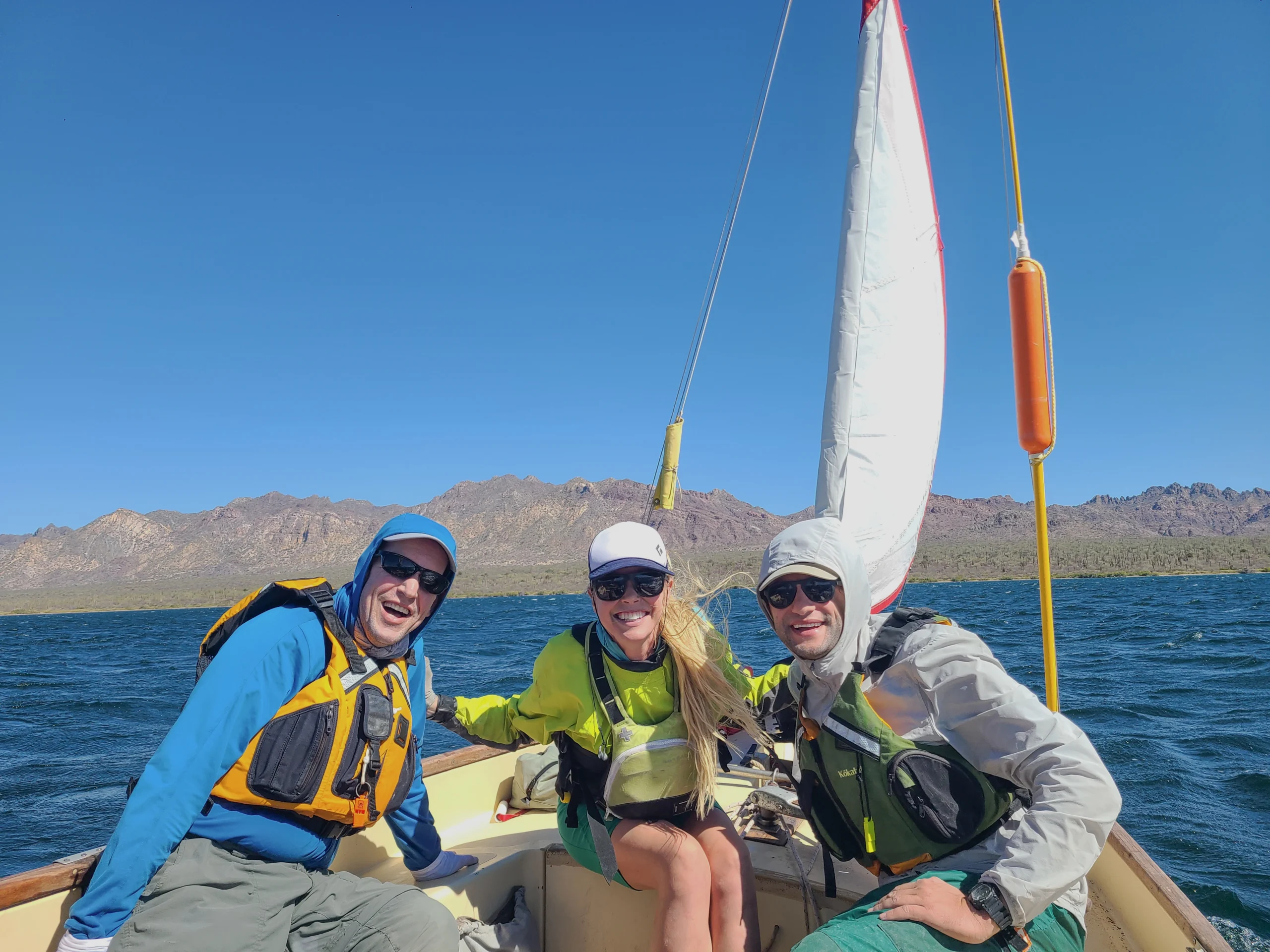 Sailors smile with mountains in the background and blue water all around.