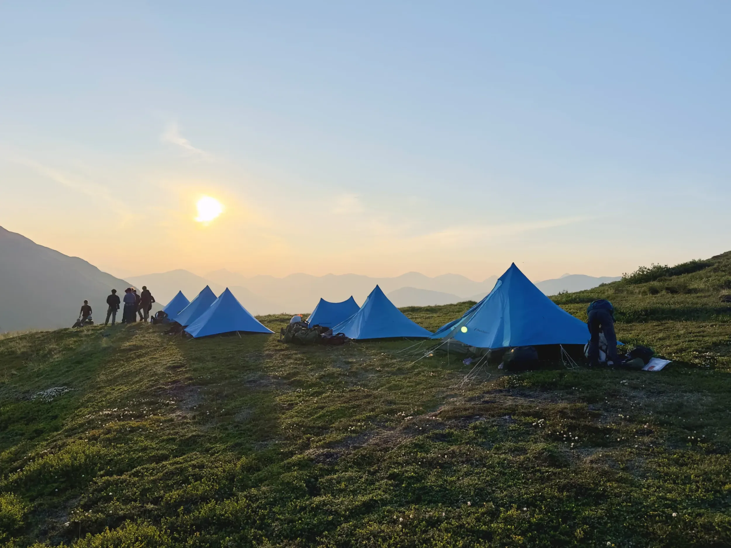 the sun sets over a group of tents.