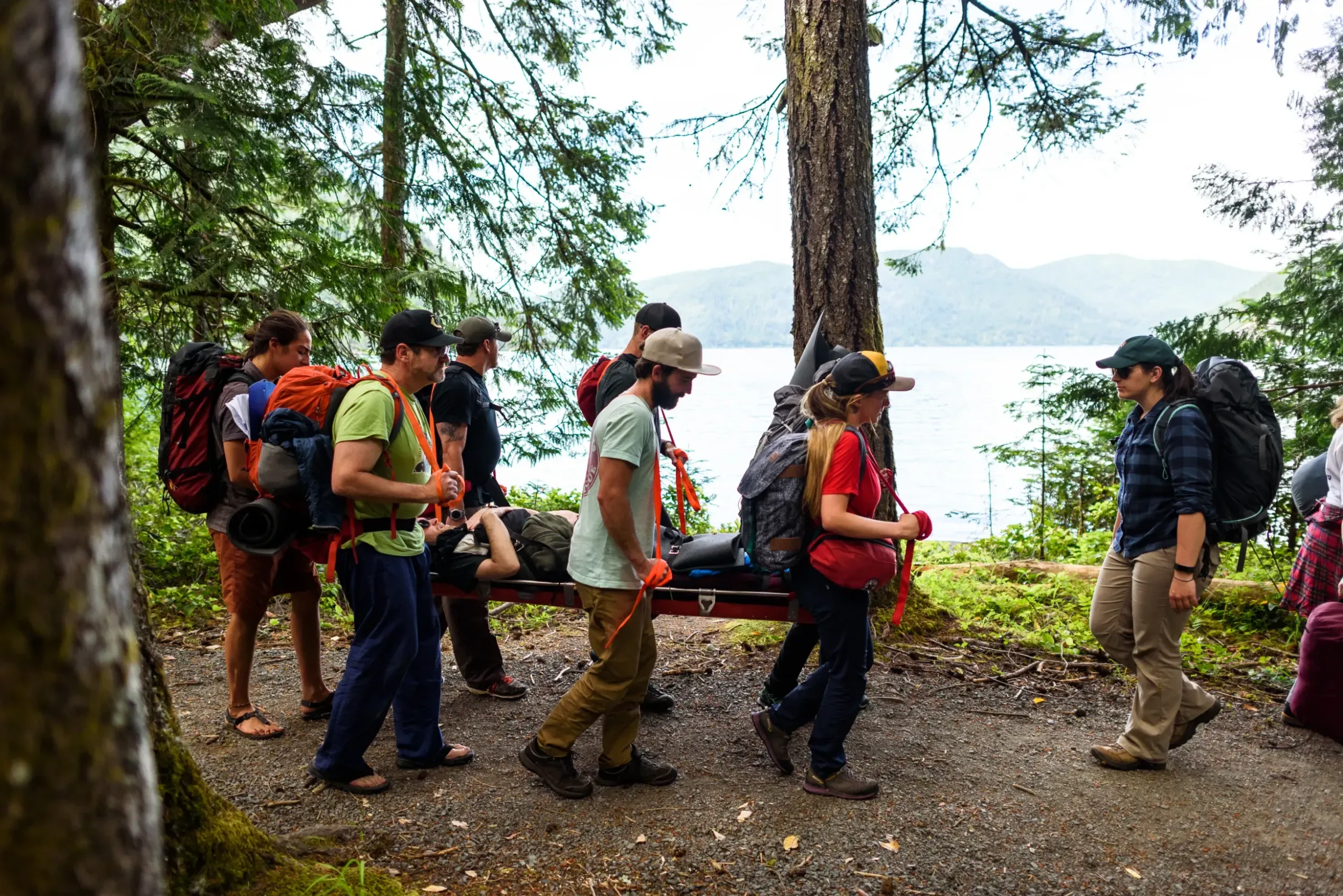 a group of people walk with a litter through a forest