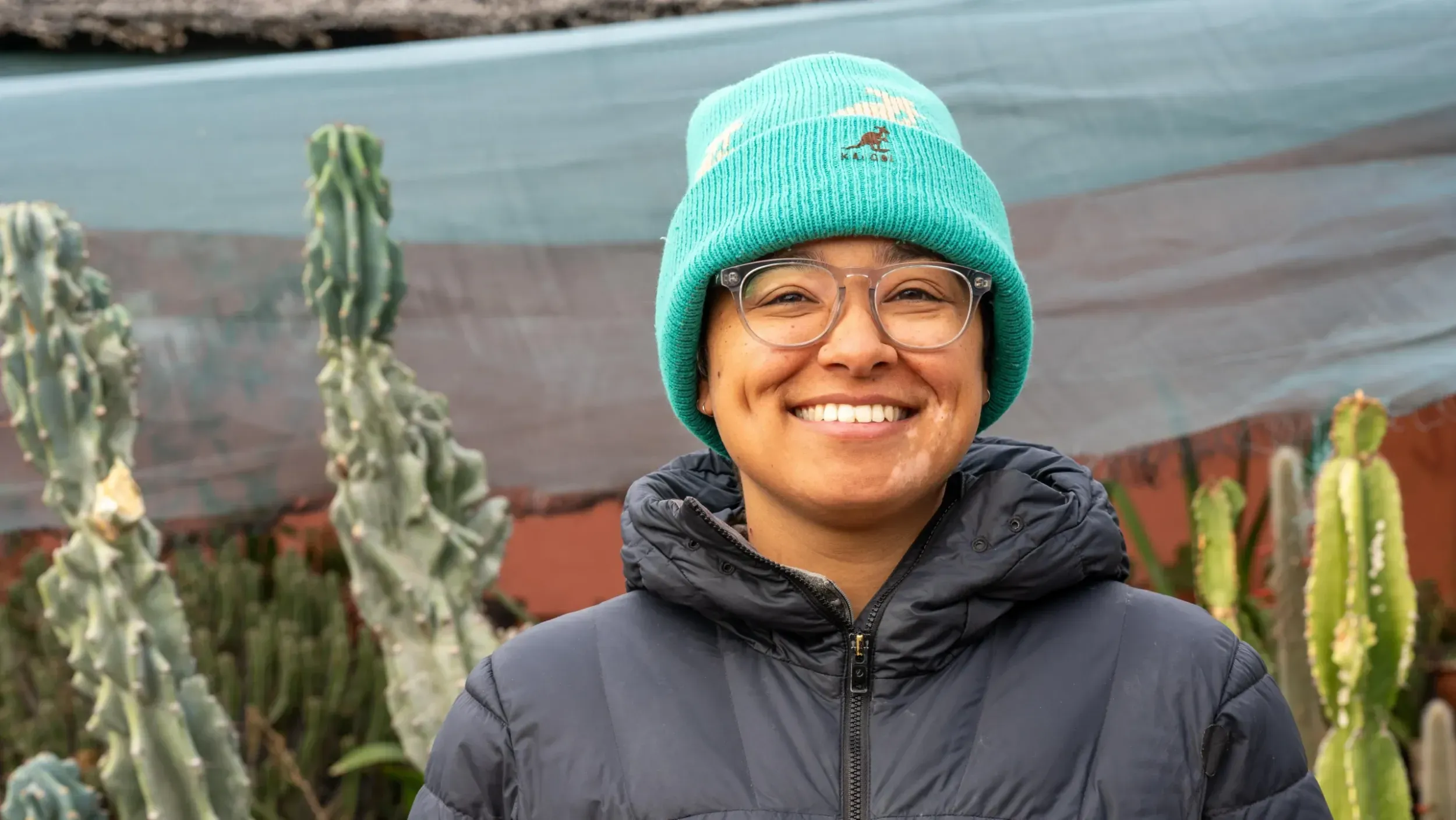 a person in a bright blue beanie and wearing glasses smiles at the camera