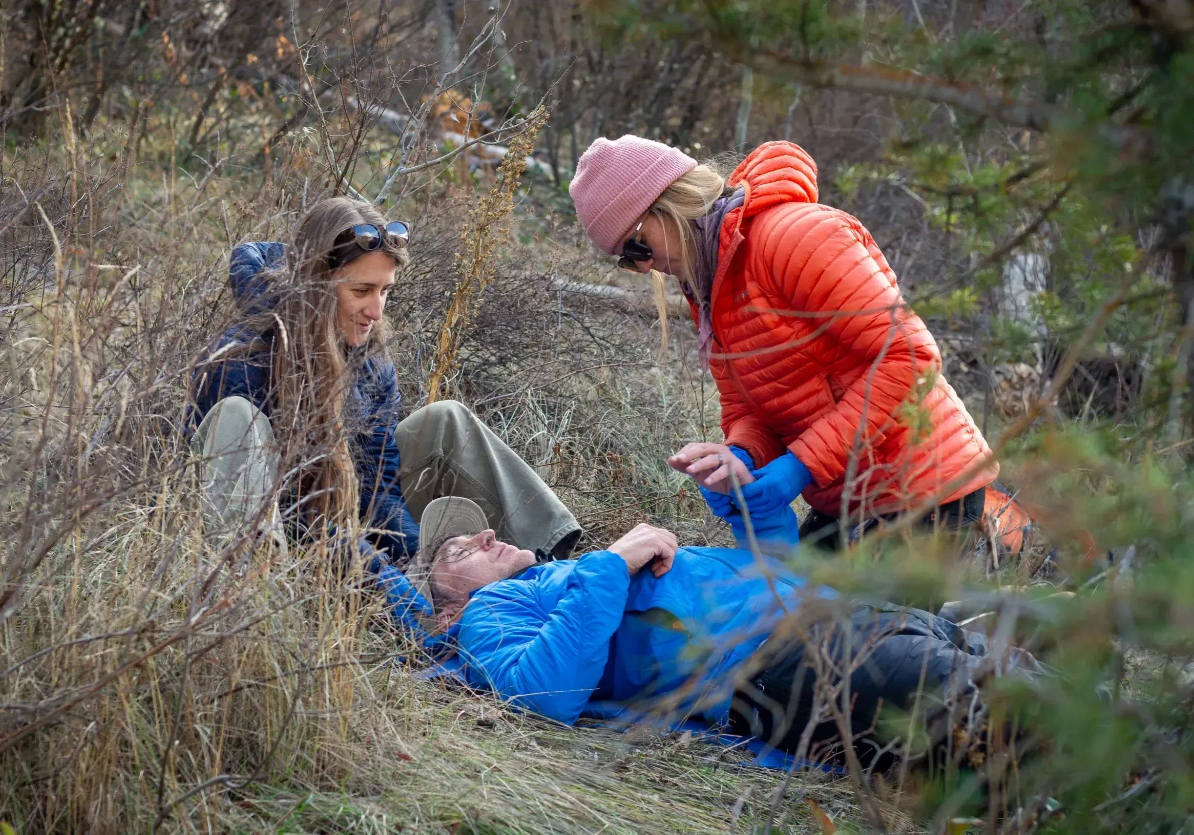 two woman in puffy jackets help a person lying on the ground